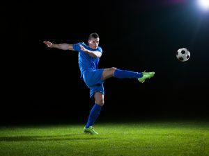 soccer player doing kick with ball on football stadium field isolated on black background