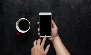 hand-using-phone-black-screen-with-cup-of-coffee-wooden-black-office-desk-table-on-top-SBI-301984858.jpgのサムネイル画像